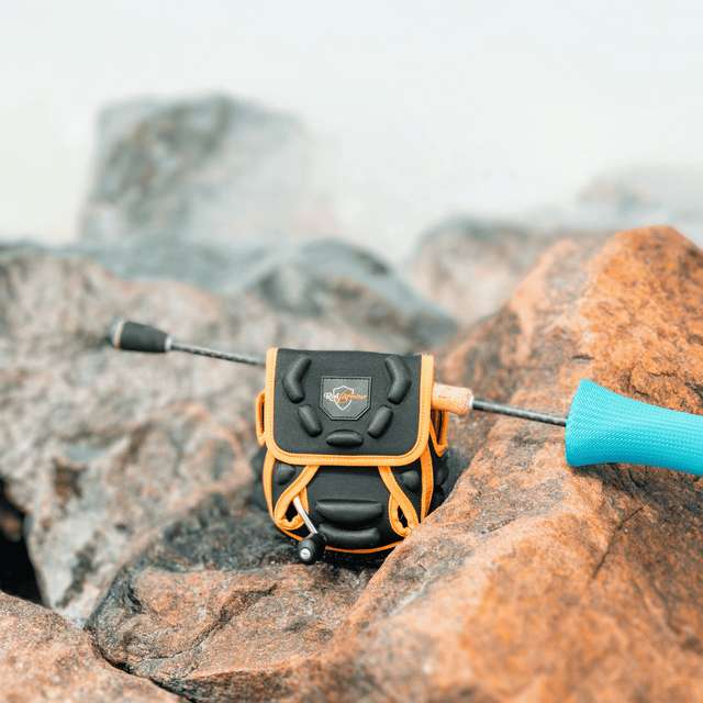 Spinning Reel Cover staged on coastal rocks beside a rod tip and blue reel handle