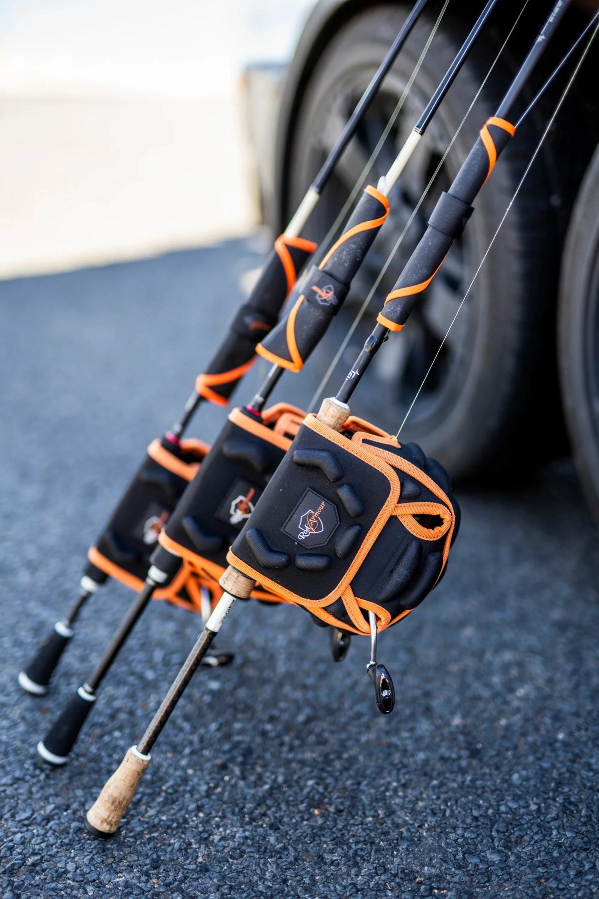 Three rigged spinning rods leaning on a car, each reel in a Reel Armour cover